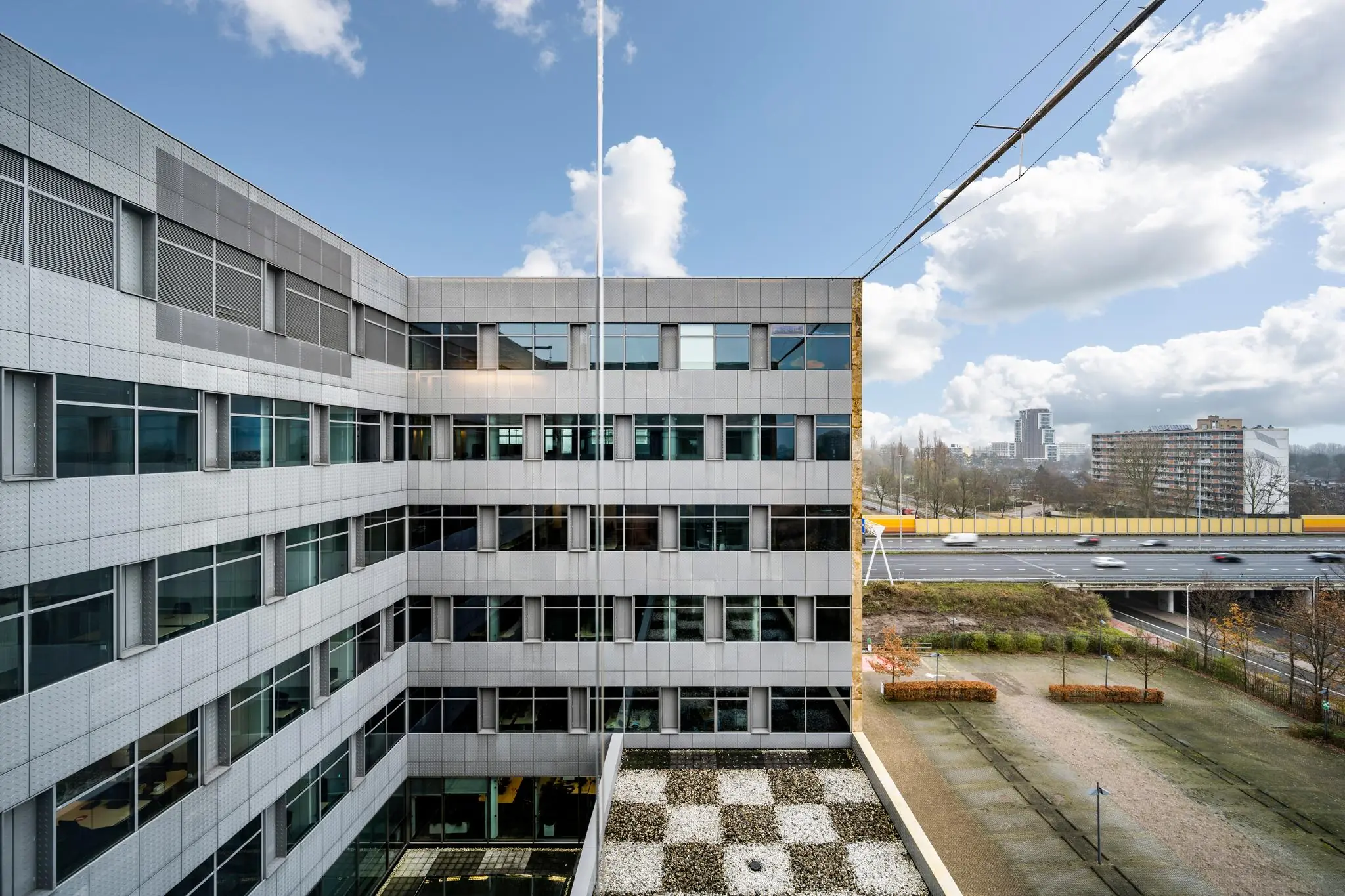Kantoorgebouw aan de Burgemeester Rijnderslaan met uitzicht op snelweg en woonflats in de verte.